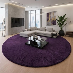 Puede incluir: Una alfombra redonda de color morado intenso con pelo largo y textura densa. La alfombra está colocada sobre un suelo de madera clara y sirve como base central para una mesa de centro de cristal y un sofá seccional gris claro en la sala.