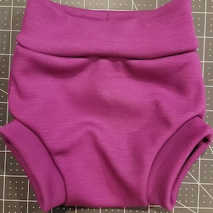 May include: Magenta cloth diaper covers with a wide, folded waistband and leg cuffs. The diaper covers are made of a soft, stretchy material and are designed to fit snugly. The diaper covers are designed for babies and toddlers.
