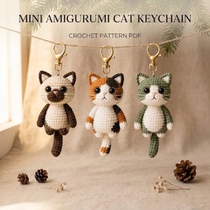 May include: Three mini amigurumi cat keychains hanging from a string, featuring a Siamese-style cat, a calico cat, and a green and white cat. Each crochet cat has black eyes, a pink nose, and a gold-tone metal lobster clasp keychain attachment.