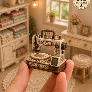 Op de afbeelding: Een miniatuur naaimachinemodel met een crèmekleurige behuizing met bloemaccenten, vier kleine garenklosjes aan de bovenkant en een ronde borduurring als basis. De machine toont de tekst Stitching Memories en een STL DIGITAL FILE badge.