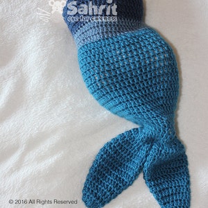 May include: A crocheted baby mermaid tail in shades of blue. The tail features a dark blue waistband that fades into lighter blues, with a detailed fin design. The text "Sahrit eye for cuteness" is visible. The copyright notice "© 2016 All Rights Reserved" is also visible.