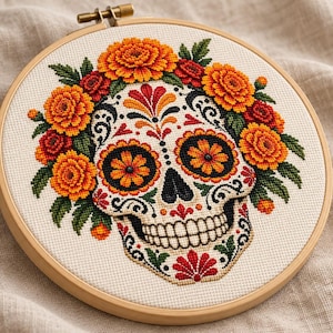 May include: A cross-stitch embroidery in a round wooden hoop featuring a white skull decorated with intricate black, red, and yellow patterns. The skull is surrounded by a vibrant crown of orange and yellow marigold flowers and green leaves.