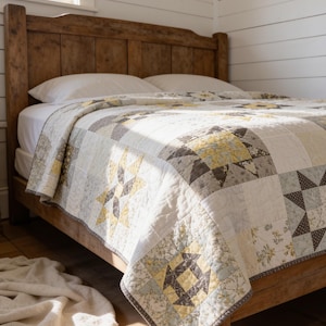 May include: A patchwork quilt featuring a repeating star pattern in shades of yellow, grey, and white. The quilt is constructed from various fabric squares with floral and geometric prints, finished with a thin grey border and visible stitching.