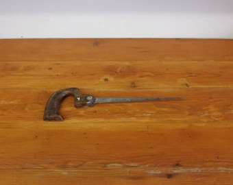 May include: A vintage hand saw with a wooden handle and a metal blade. The saw is lying on a wooden surface.