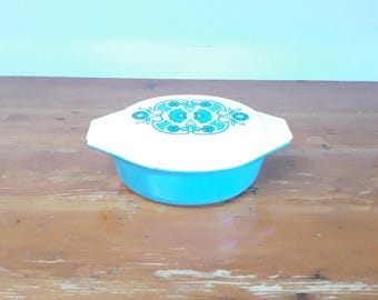 May include: A vintage turquoise and white casserole dish with a lid. The lid features a floral design in shades of turquoise. The dish is a bright turquoise colour and has a white lid with handles. This retro kitchenware is perfect for serving.