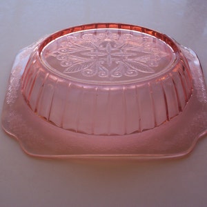 May include: A pink glass bowl with a scalloped edge and a floral design on the bottom.
