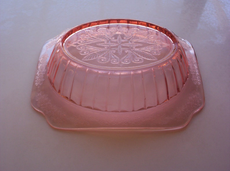 May include: A pink glass bowl with a scalloped edge and a floral design on the bottom.