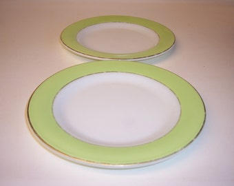 May include: Two white ceramic plates with a light green rim and a gold accent. The plates are different sizes.