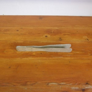 May include: A wooden pair of tongs with a light gray finish. The tongs are lying flat on a wooden surface.