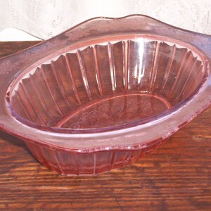 May include: A pink glass bowl with a fluted design and a scalloped edge. The bowl has a delicate floral pattern etched into the glass.