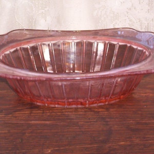 May include: A pink glass bowl with a ribbed design. The bowl is oval shaped and has a slightly scalloped edge.