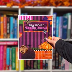 May include: A rectangular reading journal with a purple and black striped background, featuring the text 'cozy autumn reading journal' in a central frame. The design includes orange pumpkins, autumn leaves, and animal print accents.