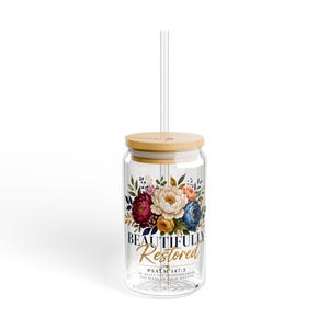Peut inclure: Un gobelet en verre transparent avec un couvercle en bambou et une paille transparente. Le verre présente un bouquet floral dans des tons de rouge, blanc, bleu et jaune, avec le texte "BEAUTIFULLY Restored" et "PSALM 147:3 HE HEALS THE BROKENHEARTED AND BINDS UP THEIR WOUNDS."