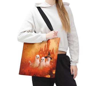 Könnte beinhalten: Eine Tragetasche mit einer leuchtend orangefarbenen Halloween-Illustration von drei weißen Geistern, von denen einer einen schwarzen Hexenhut trägt, vor einer Kulisse aus einem gruseligen Schloss, kahlen Ästen und kleinen Kürbissen.