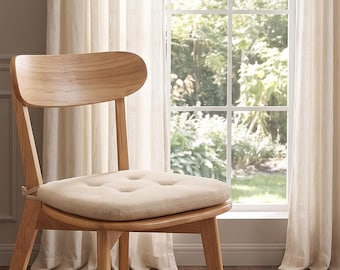 May include: A light-toned wooden chair featuring a curved backrest and four tapered legs. The seat is topped with a square, beige tufted cushion that is secured to the frame with thin ties at the back, providing a simple and functional seating design.