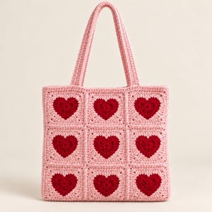 May include: A square-shaped crochet tote bag featuring a grid pattern of nine individual granny squares. Each square displays a deep red heart centered within a light pink background. The bag includes two matching light pink crochet handles.