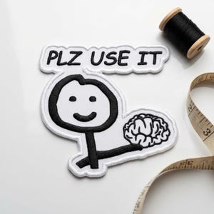 May include: A white embroidered patch featuring a black stick figure holding a brain, with a speech bubble above containing the text PLZ USE IT in black embroidery. The patch is positioned near a black thread spool and a measuring tape.