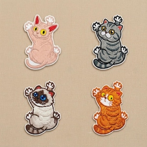 May include: Four embroidered cat patches featuring different coat colors and patterns. One is light pink, one is grey striped, one is a cream and brown color-point, and one is orange striped. Each cat is depicted in a sitting pose with raised paws.