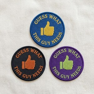 May include: Three circular embroidered patches featuring a thumbs-up icon in the center. The top patch is blue with gold text and icon. The bottom left is black with orange text and icon. The bottom right is purple with light green text and icon.