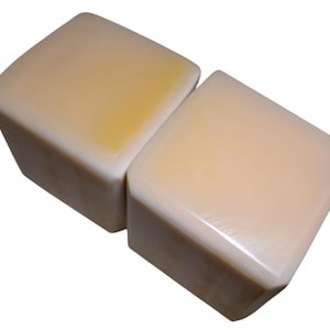 Puede incluir: Dos objetos cúbicos lisos de color blanco roto con una apariencia sólida y densa. Cada cubo presenta una superficie ligeramente pulida con sutiles variaciones de tono, que van del blanco crema al amarillo pálido, y bordes redondeados.