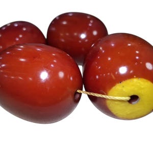 May include: Four smooth, oval-shaped beads with a deep reddish-brown, polished finish. Each bead features a central hole for stringing. One bead displays a distinct, bright yellow circular accent around its opening, connected by a thin cord.