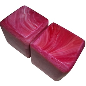 May include: Two square-shaped blocks featuring a vibrant magenta and white marbled pattern. The surfaces display a smooth, glossy finish with swirling colour variations throughout each cube, creating a distinct visual texture on all visible sides.