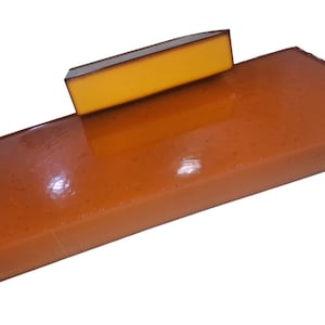 May include: A rectangular block of smooth, amber-coloured resin with a glossy finish, featuring a smaller, thinner rectangular piece of solid yellow material resting on top, both displaying clean, sharp edges and a uniform, solid appearance.