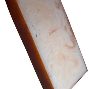 Può includere: Un blocco rettangolare caratterizzato da un lato solido color ambra scuro e una faccia piatta con un motivo marmorizzato vorticoso nei toni del bianco crema e del pesca tenue. La superficie appare liscia e lucida, mostrando una miscela di resina opaca e traslucida.