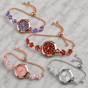May include: Four analog wristwatches with round faces and adjustable chain bracelets. Three watches feature rose gold-tone metal with purple, red, and pink crystal accents. One watch features silver-tone metal with clear crystal accents.
