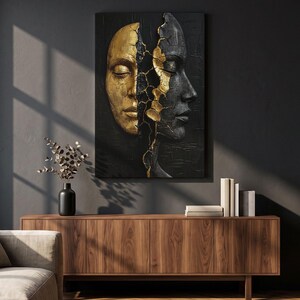 May include: A rectangular wall art piece featuring a split face design. The left side is metallic gold with a smooth finish, while the right side is matte black with a textured surface. A jagged, cracked line runs down the centre in gold.