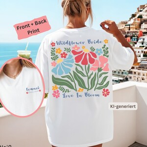 Könnte beinhalten: Ein weißes T-Shirt mit einem großen, bunten Blumenmotiv auf der Rückseite und dem Text Wildflower Bride sowie Love In Bloom. Auf der Vorderseite steht der Text Franzi Ibiza 2026 mit einer kleinen Blume. Das Design ist in Blau, Rot und Rosa.