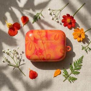 May include: A rectangular protective case for wireless earbuds featuring a vibrant, swirling pattern of red and orange hues. The case has a smooth, glossy finish and a small circular cutout on the side for a lanyard or attachment point.