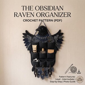May include: A black raven-shaped wall organiser crochet pattern PDF titled THE OBSIDIAN RAVEN ORGANISER. The wall hanging features nine black pockets, three metal hooks, and textured wings. It holds a tube, a bottle, a notebook, and keys.
