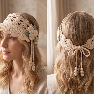 May include: A beige crochet visor featuring an intricate openwork pattern on the brim and a decorative cluster of three white flowers with green leaves on the side. The back includes a crocheted tie closure with two dangling braided cords.