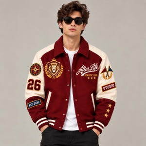 May include: A burgundy and cream varsity jacket worn over a white t-shirt. The jacket features various embroidered patches, including a lion crest, a compass, the text After Life Athletic Club, the number 26, the text EST. 2026, STUDIO, and three stars.