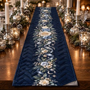 May include: A navy blue quilted table runner featuring a central vertical print of white and blue roses, green pine sprigs, silver ribbons, and small ornaments. The fabric has a textured herringbone pattern throughout the dark blue background.