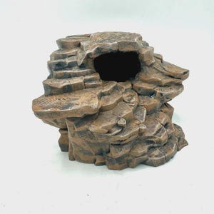 Könnte beinhalten: Ein braunes, strukturiertes Versteck in Felsform für Kleintiere mit einer geschichteten, zerklüfteten Oberfläche und einer markanten, dunklen, hohlen Öffnung in der Mitte. Die Struktur wirkt realistisch und verwittert mit tiefen Spalten.