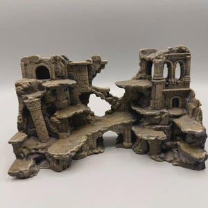 May include: A tan and grey aquarium ornament featuring a multi-level structure with weathered stone textures, arched doorways, carved pillars, and various flat platforms. The piece displays a ruined architectural design with intricate details.