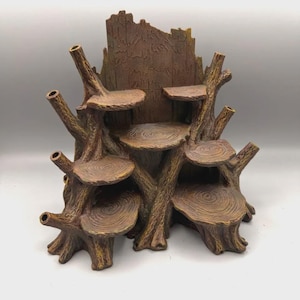 Op de afbeelding: Een bruine, boomstronk-vormige displaystandaard met meerdere ronde, platte plateaus die lijken op jaarringen op verschillende hoogtes. De structuur heeft een textuur die lijkt op boomschors en diverse holle, takachtige uitsteeksels.