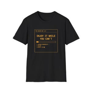 May include: A black short-sleeved t-shirt featuring a yellow graphic box with the text THE GOLDEN AGE v1.0, ENJOY IT WHILE YOU CAN'T, a loading bar, and the lines LOADING PROSPERITY, FAILED, and RETRY? Y/N with a blinking cursor underscore.