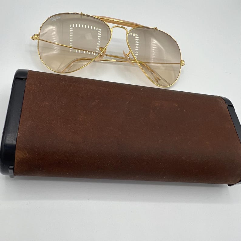 May include: Gold aviator sunglasses with brown tinted lenses and a brown leather case.