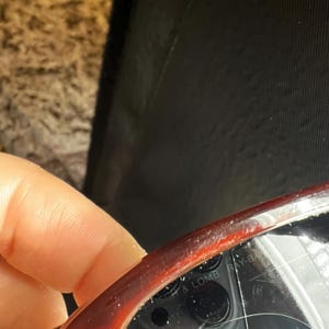 May include: Close-up of a pair of Ray-Ban sunglasses with a dark red frame. The brand name, Bausch & Lomb, is visible on the frame. The lenses are not visible in the image.