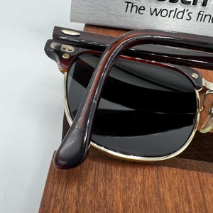 May include: Close-up of sunglasses with dark lenses and a brown tortoiseshell frame. The sunglasses have a gold-colored metal rim and are resting on a wooden surface. The text "The world's fine" is visible in the background.