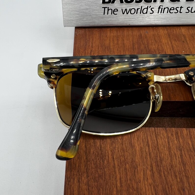 May include: Sunglasses with a tortoiseshell pattern on the frames and temples. The lenses are a dark brown color, and the frames have a gold-colored metal rim. The text "The world's finest su..." is visible at the top.