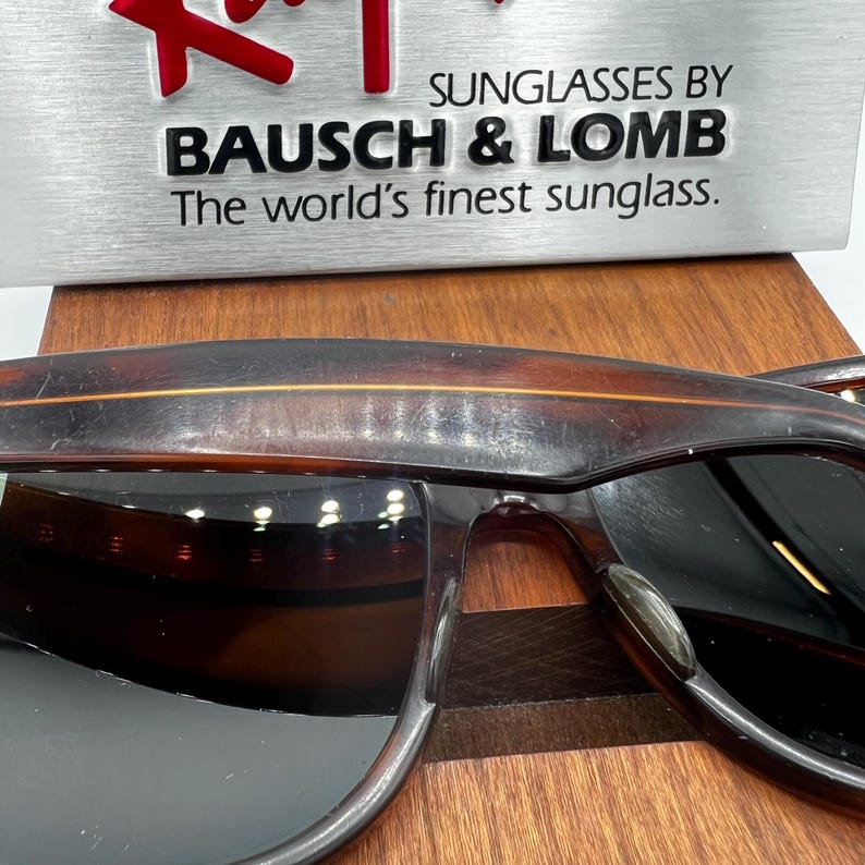 May include: Sunglasses by Bausch & Lomb with a brown tortoiseshell frame. The lenses are dark, and the frame has a classic design. The text "The world's finest sunglass" is visible.