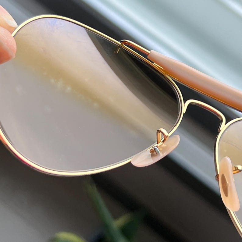 May include: Gold aviator sunglasses with brown tinted lenses and a pink nose bridge.
