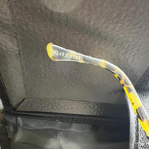 May include: Close-up of a pair of eyeglasses with a tortoise shell pattern on the arm. The text "W1483 VTAR" is printed on the arm. The glasses are in a black case.