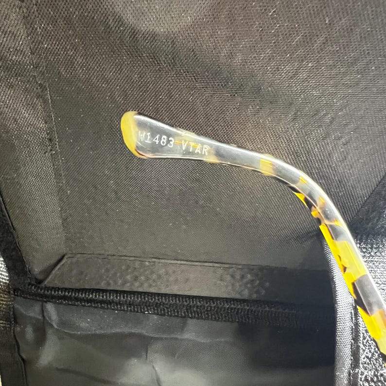 May include: Close-up of a pair of eyeglasses with a tortoise shell pattern on the arm. The text "W1483 VTAR" is printed on the arm. The glasses are in a black case.