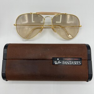 May include: Gold aviator sunglasses with brown lenses and a brown leather case with the Ray-Ban logo and the text "BAUSCH & LOMB FANTASEES".