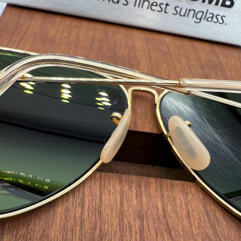 K&ouml;nnte beinhalten: Goldene Aviator-Sonnenbrille mit gr&uuml;nen Gl&auml;sern und Nasenpads. Die Sonnenbrille ist zusammengeklappt.